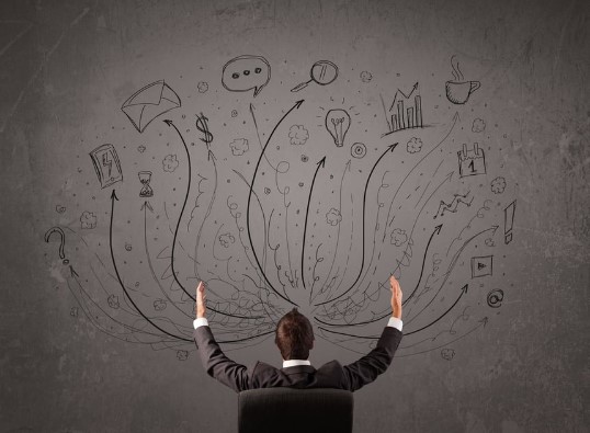 Young businessman sitting and deciding in front of a chalkboard with sketched arrows and signs in different directions