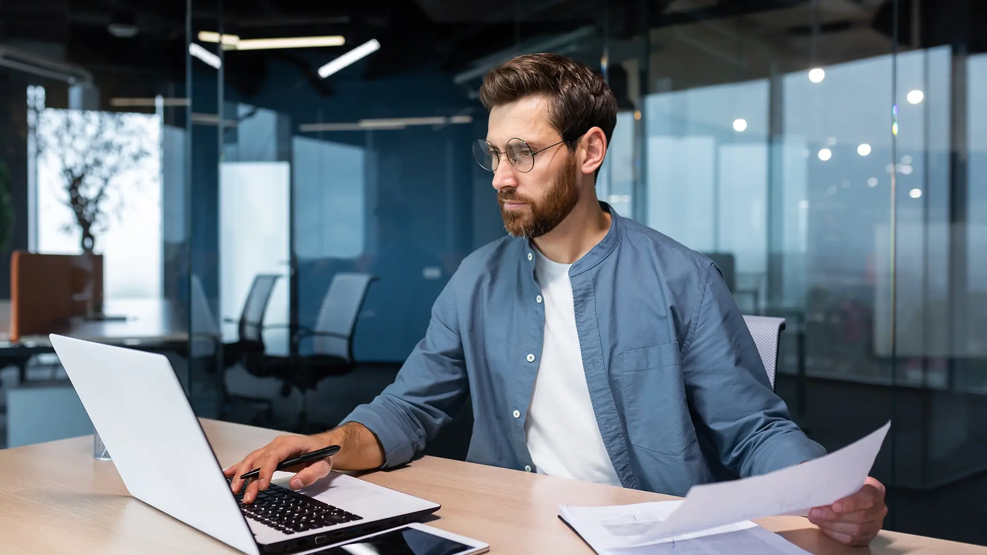 Person working on laptop with paperwork, looking focused.